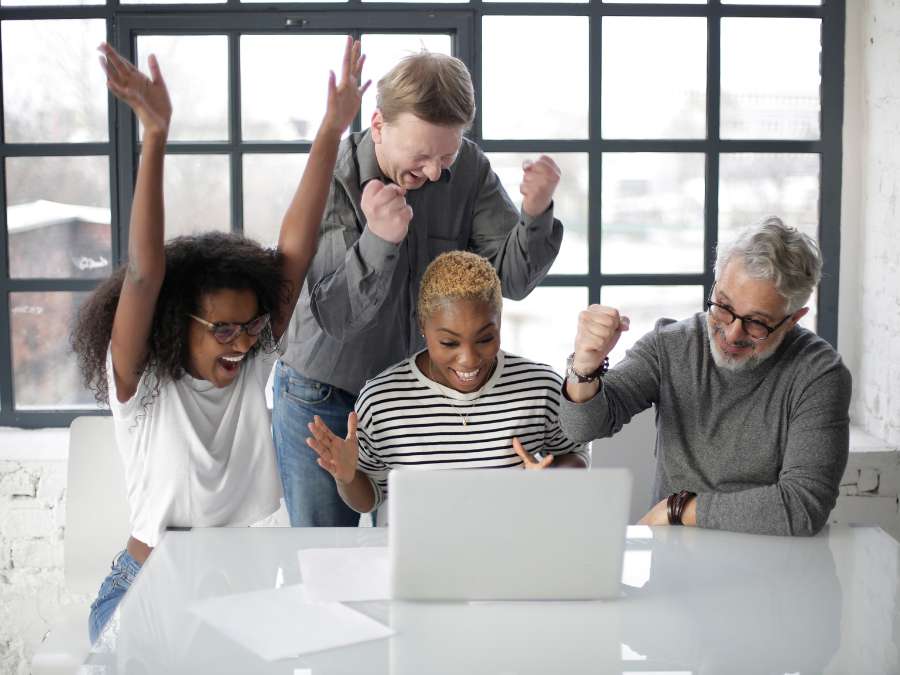 Excited multiracial colleagues enjoying triumph together in front of laptop in office